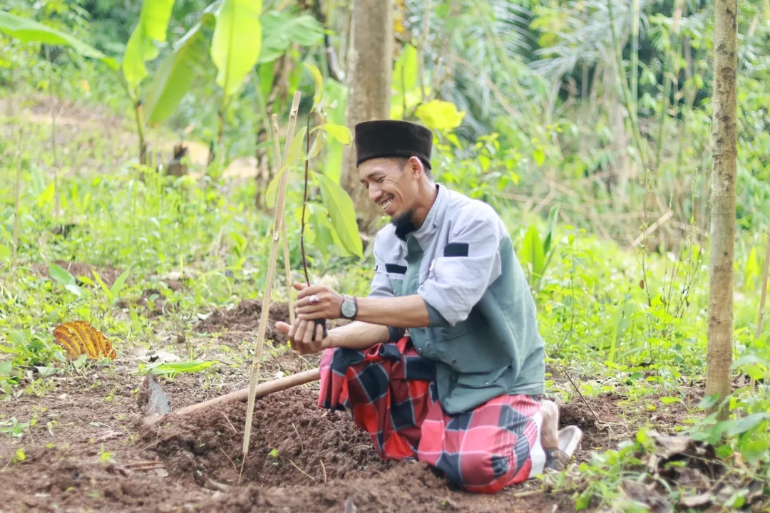 A man kneeling to plant a small tree sapling in a lush green forest at a Mission reforestation site