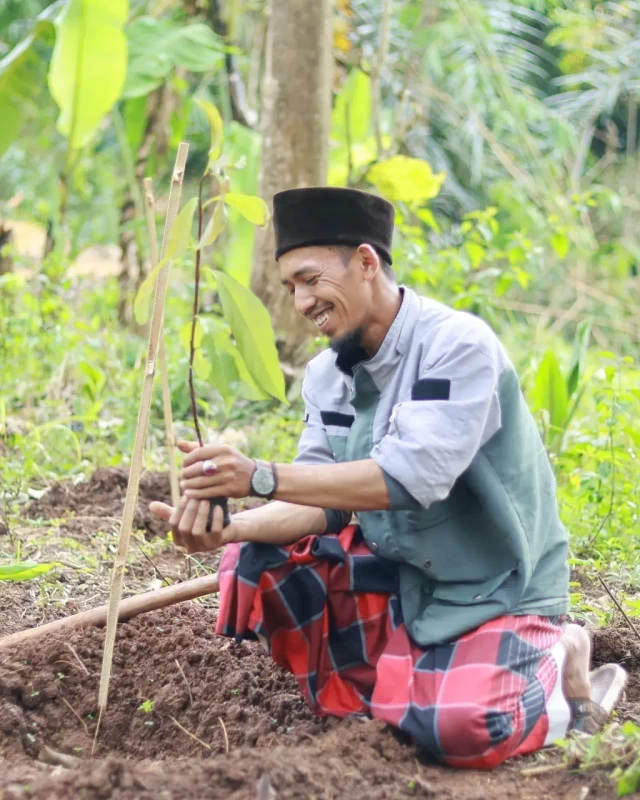 A man kneeling to plant a small tree sapling in a lush green forest at a Mission reforestation site